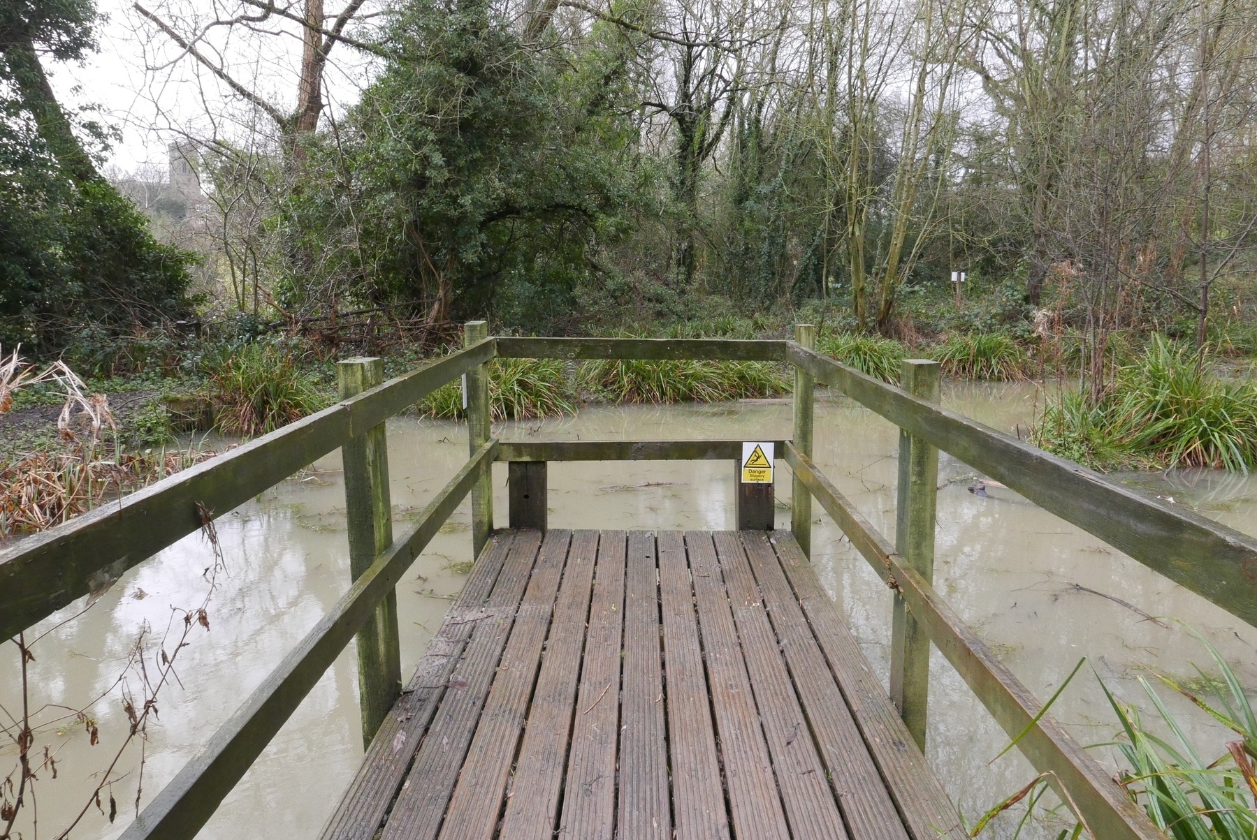 A short walkway over a cloudy pool in the woods, with a church in the distance