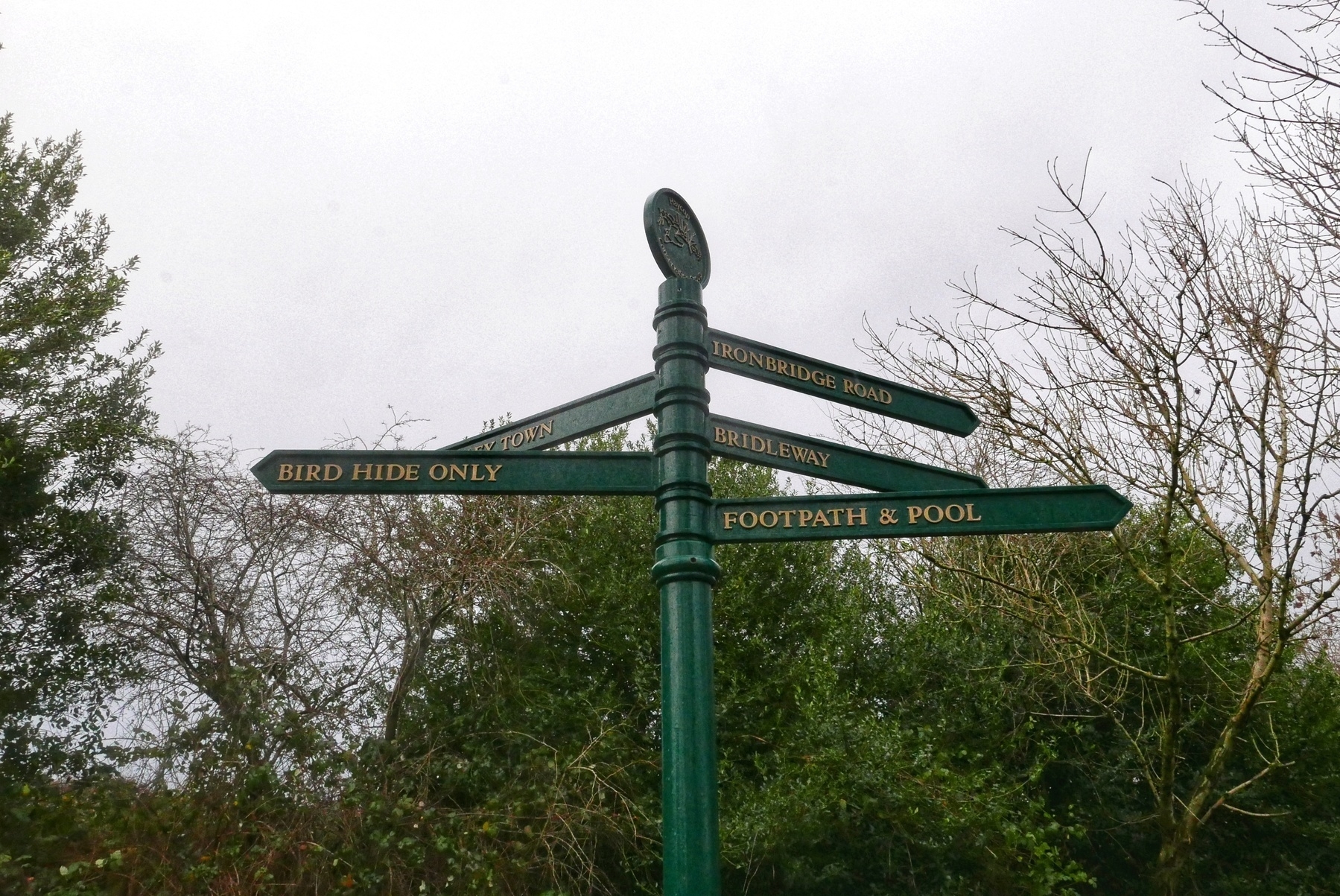 Green iron signpost with gold lettering for footpaths with "Bird hide only", "Bridleway", a town, "Ironbridge road", and "Footpath and pool"