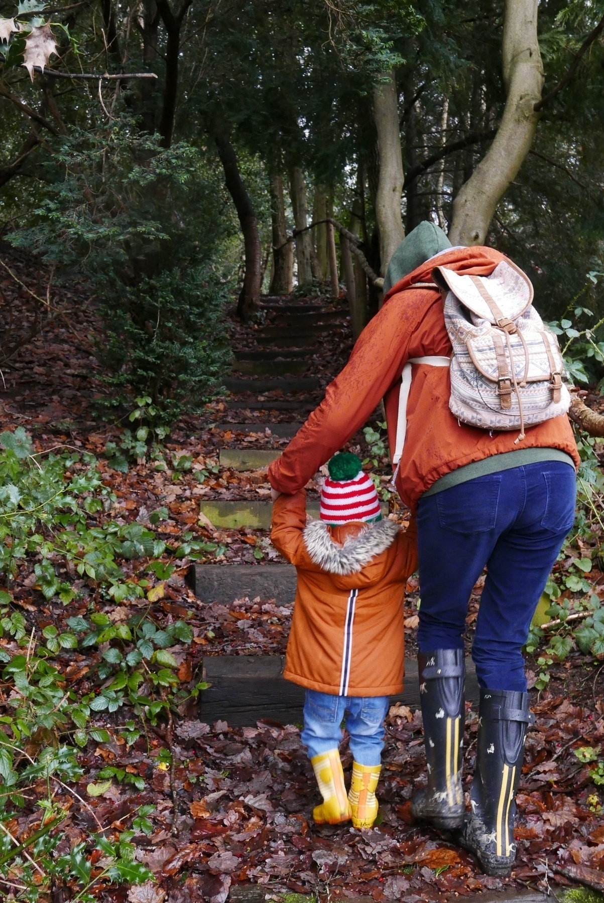 Little one and his mother climbing some steps in a wooded area