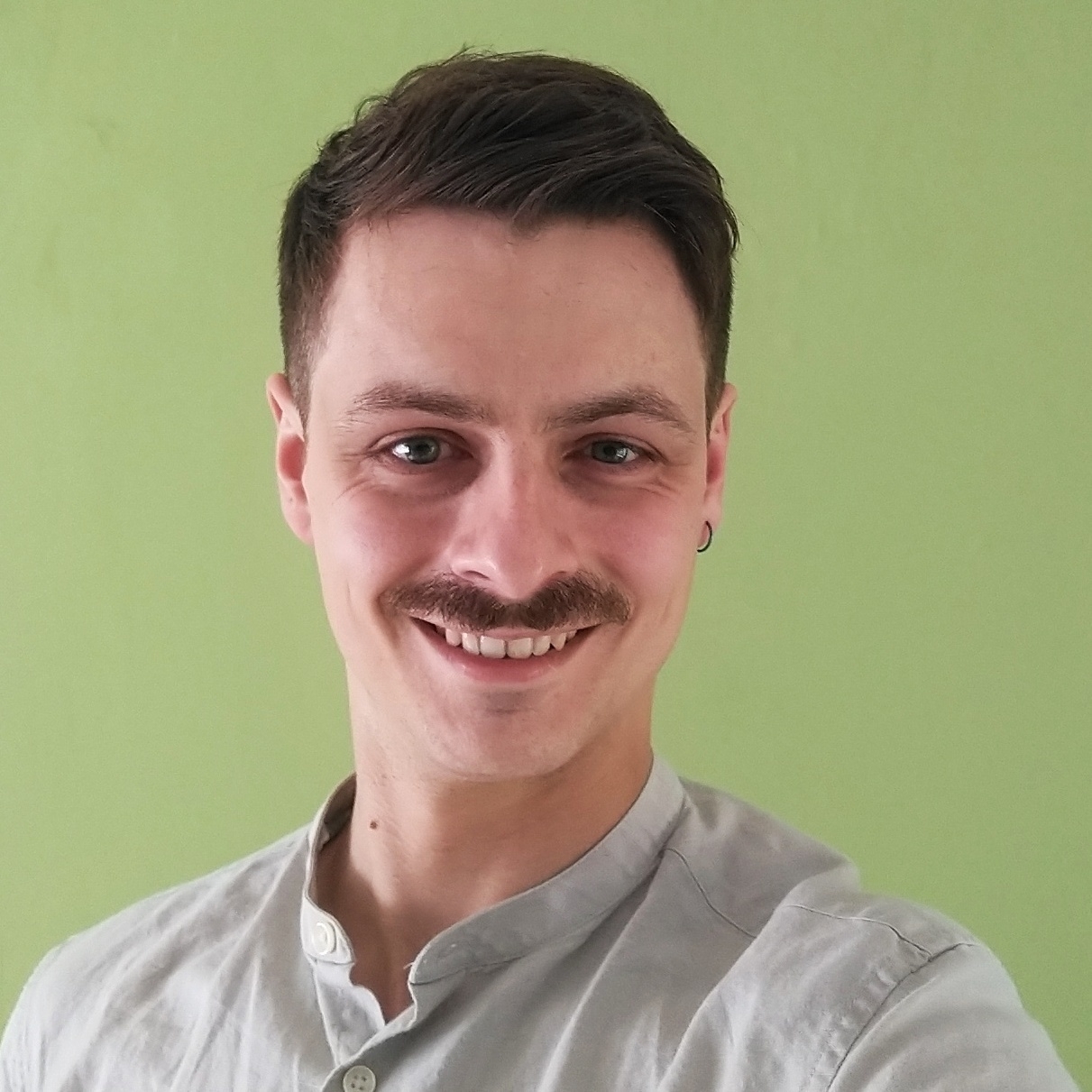 A picture of me. I am a 32-year-old white man with short brown hair and a short moustache. I have an earring and am wearing a collarless linen shirt